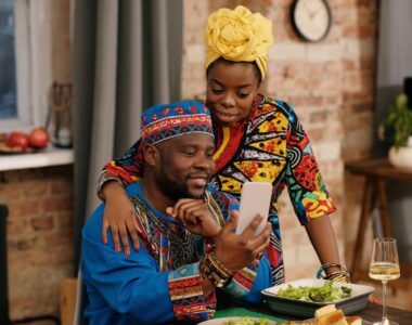 A joyful couple in colorful dashiki attire making a video call at a festive indoor gathering.