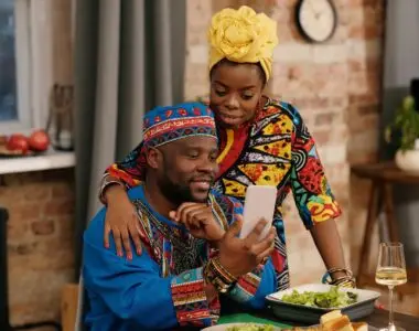 A joyful couple in colorful dashiki attire making a video call at a festive indoor gathering.