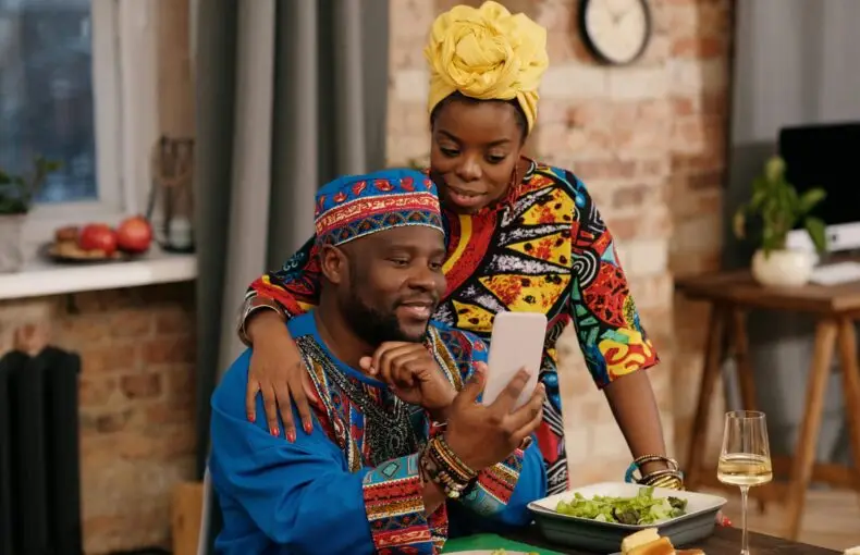 A joyful couple in colorful dashiki attire making a video call at a festive indoor gathering.