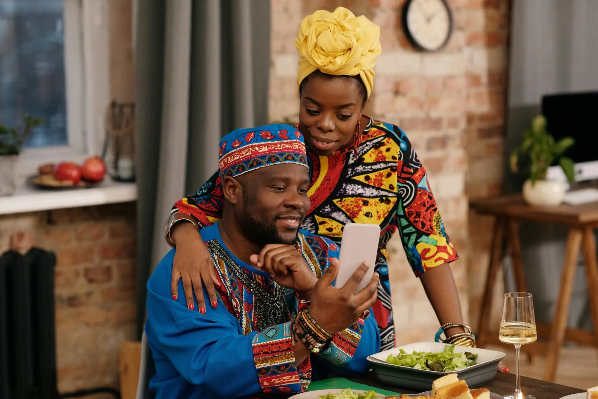 A joyful couple in colorful dashiki attire making a video call at a festive indoor gathering.